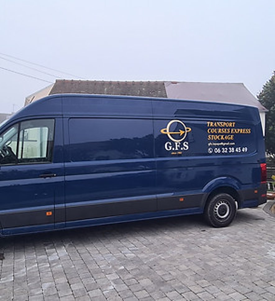 Une grande camionnette bleue portant le logo G.F.S et les mentions transport, courses express et stockage, garée sur un sol pavé.
